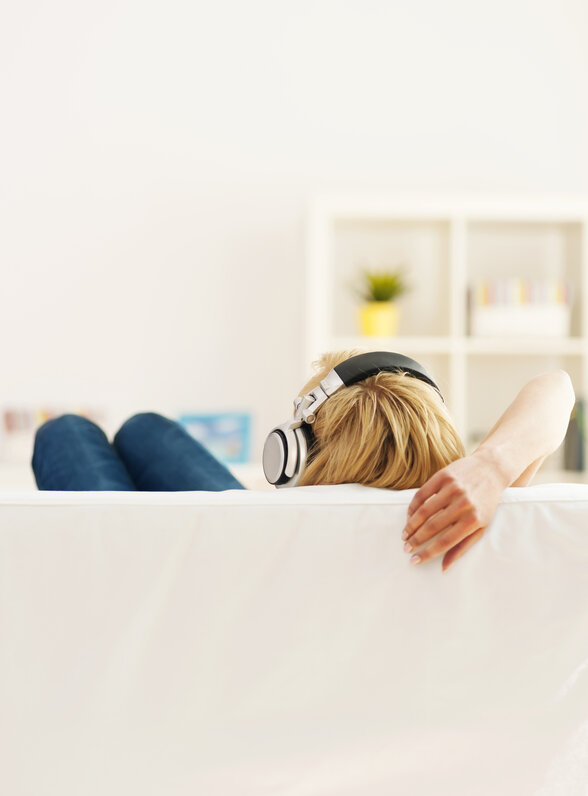 Personne allongée de dos sur un canapé blanc, écoutant de la musique avec un casque audio
