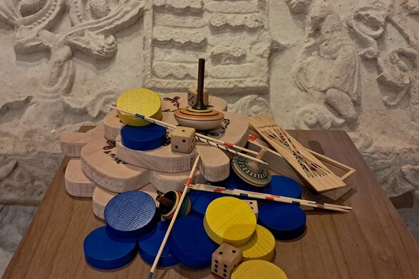 Jeux en bois anciens posés sur une table, devant un mur de pierre sculpté du Donjon