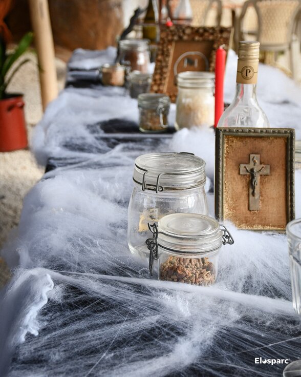 Table décorée pour Halloween avec fausses toiles d'araignée, bocaux anciens, bougie rouge et crucifix encadré