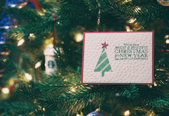 Carte de vœux faite main avec un sapin découpé, suspendue dans un sapin de Noël illuminé