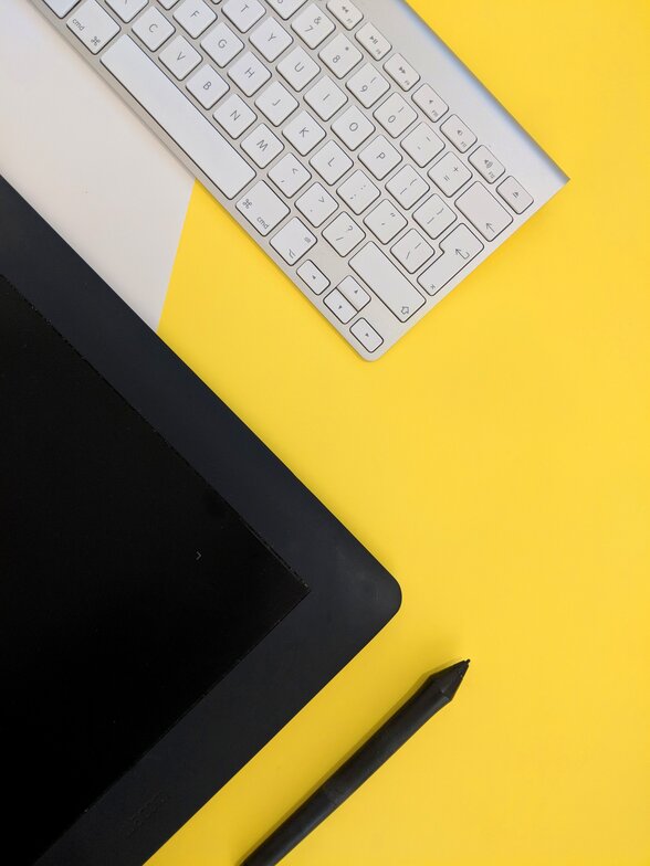 Clavier d'ordinateur, tablette graphique et stylet posés sur un fond jaune