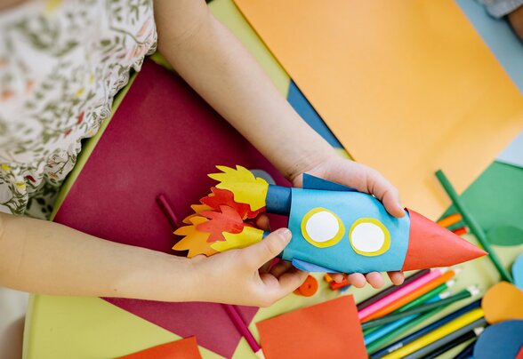 Mains d'enfant tenant une fusée en papier coloré au-dessus d'une table de bricolage