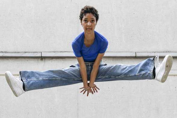 Une danseuse saute en grand écart devant un mur de béton